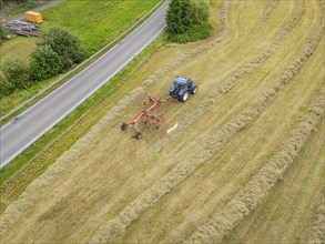 Aerial view of a tractor with hay machine in a field next to a country road, Dachtel. Black Forest,