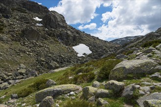 Mountainous landscape with rocky terrain and scattered patches of snow under a blue sky with