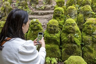 Visitor takes pictures of rakan statues at Otagi Nenbutsu-ji temple, Kyoto, Japan, Asia