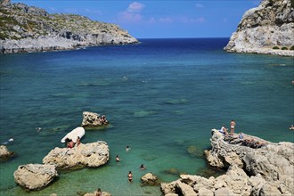 Sunbathing people on rocks on a coast with deep blue water and sunny sky, Anthony Quinn Bay, Vagies