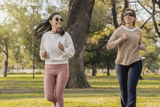 Two women are jogging side by side in a park, enjoying a sunny day outdoors. They smile as they