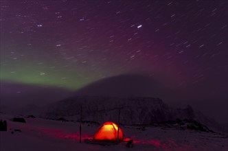 Northern Lights (Aurora borealis) and star trails above an illuminated tent in the valley Stuor