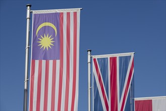 Several flags of different countries fly side by side under a clear blue sky, Malaysian flag,