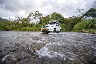 Toyota off-road vehicle with roof tent drives through a wide river in the rainforest, Alajuela