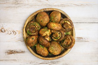 A rustic wooden plate with baked champignon mushrooms, each filled with herbs, sitting atop a light