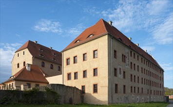 Large, historic building with light-coloured walls and red roof under a blue sky, castle, today