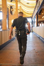 A man in safety equipment walks through an empty, well-lit wooden marquee, Canstatter Wasen,