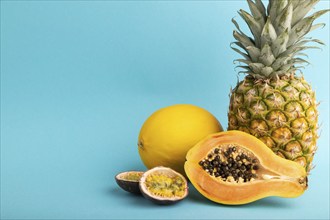 Ripe cut papaya, pineapple, melon, passion fruit, on blue pastel background. Side view, copy space.