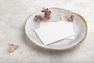 White paper invitation card, mockup with dried hydrangea flowers on ceramic plate and gray concrete