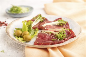 Slices of smoked salted meat with cilantro microgreen on gray concrete background and orange