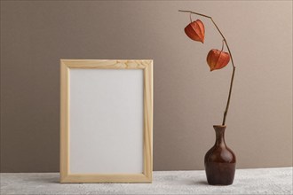 White wooden frame mockup with physalis in ceramic vase on beige paper background. Blank, vertical