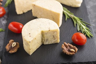 Cheddar cheese and various types of cheese with rosemary and tomatoes on black slate board on a