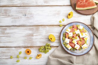 Vegetarian salad with watermelon, feta cheese, and grapes on blue ceramic plate on white wooden