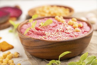 Hummus with beet and microgreen basil sprouts in wooden bowl on a white wooden background and linen