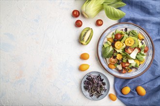 Vegetarian salad of pac choi cabbage, kiwi, tomatoes, kumquat, microgreen sprouts on a white