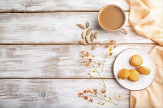 Orange macarons or macaroons cakes with cup of apricot juice on a white wooden background and