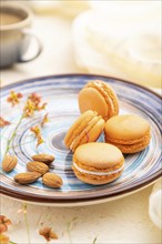 Orange macarons or macaroons cakes with cup of coffee on a white concrete background and linen