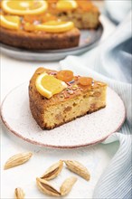 Orange cake with almonds and a cup of coffee on a white concrete background and blue linen textile.