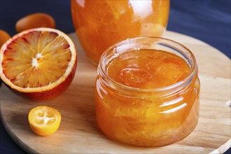 Orange and kumquat jam in a glass jar with fresh fruits on a wooden kitchen board. Homemade, close