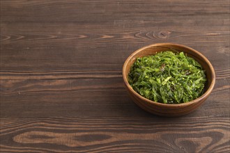 Chuka seaweed salad in wooden bowl on brown wooden background. Side view, copy space