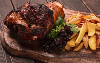 Pork knuckle, in soy-honey sauce, with fried potatoes, on a wooden chopping board, homemade, no