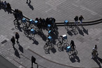 Bicycles and drivers of the food delivery service WOLT at their meeting point, passers-by,