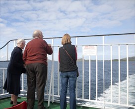 Three people looking back to the island from a Caledonian MacBrayne ferry ship leaving Barra, Outer