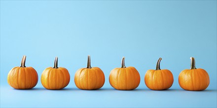 Small orange pumpkins in a row on light blue background. Generative Ai, AI generated