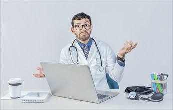 Doctor with laptop with confused expression, clueless raising arms. Young doctor using laptop with