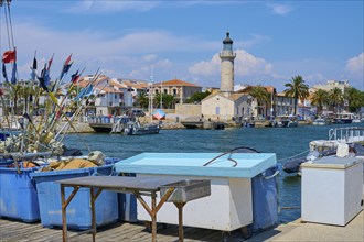 Coastal town with colourful houses and palm trees, boats in the water and a lighthouse, on a sunny