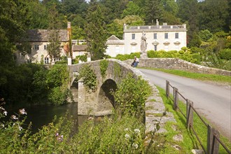 Bridge crossing the River Frome and the classical Georgian facade of Iford Manor, near Freshford,