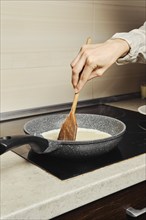 Unrecognizable woman miking scrambled eggs in a frying pan in her kitchen