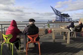 People sitting outside cafe viewing area for Port of Felixstowe, Suffolk, England, UK