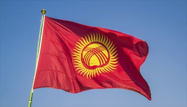 The flag of Kyrgyzstan, Kyrgyzstan, flutters in the wind, isolated against a blue sky, Asia