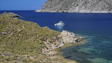 A boat lies on the turquoise sea next to a rocky shore in fine weather, Psili Ammos Srand, Patmos,