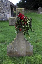 Family headstone in church graveyard decorated with holly for Christmas, Shottisham, Suffolk,