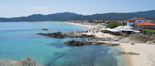 Wide coastal landscape with turquoise water and mountains in the background, lined with beaches,