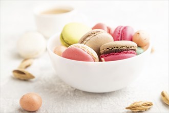 Multicolored macaroons and chocolate eggs in ceramic bowl, cup of coffee on gray concrete