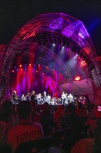 Large concert on an illuminated stage with orchestra, surrounded by an impressed audience,