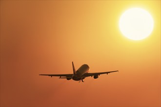 An aeroplane flies in the sunrise sky, surrounded by intense orange tones, passenger plane after