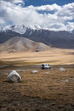 Off-road vehicle on a gravel track, glaciated and snow-covered peaks, Ak Shyrak Mountains, near