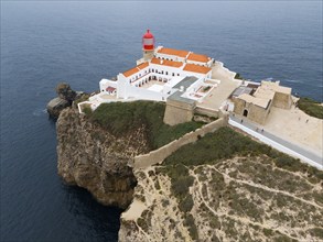 A red lighthouse on a cliff above the ocean, surrounded by white buildings and a picturesque