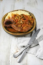 A wooden plate of osso buco served with mashed potatoes, cooked in a tomato and onion sauce with