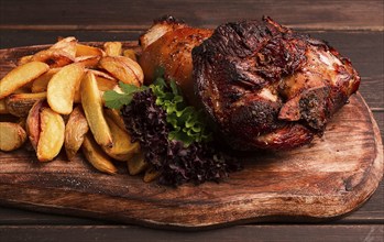 Pork knuckle, in soy-honey sauce, with fried potatoes, on a wooden chopping board, homemade, no