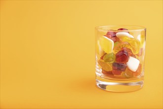 Various fruit jelly candies in drinking glass on orange pastel background. side view, copy space