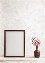 Wooden frame with purple barrenwort flowers in ceramic vase on gray concrete background. side view,