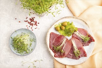 Slices of smoked salted meat with cilantro microgreen on gray concrete background and orange