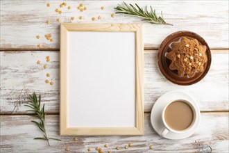 White wooden frame mockup with cup of coffee and cake on white wooden background. Blank, top view,