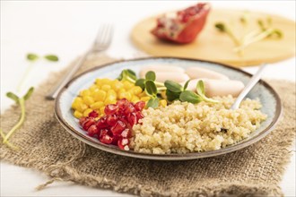 Mixed quinoa porridge, sweet corn, pomegranate seeds and small sausages on white wooden background.