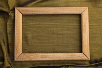 Wooden frame on smooth olive and golden silk tissue. Top view, flat lay, natural textile background